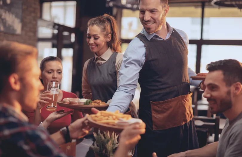 Serveuse et serveur souriant en amenant les plats pour leurs clients